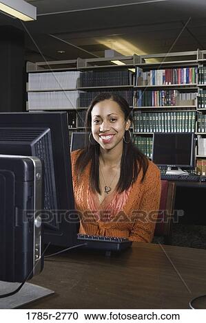 Stock Image - Young woman using a computer in the library. Fotosearch