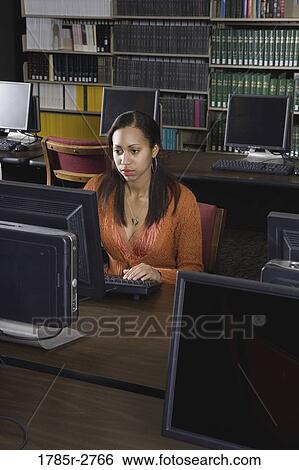 Young woman using a computer in the library View Large Photo Image Stock Photograph - Young woman using a computer in the library. Fotosearch