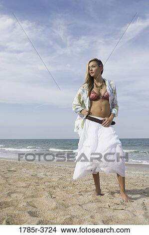 Picture - Young woman with open shirt standing on the beach. Fotosearch