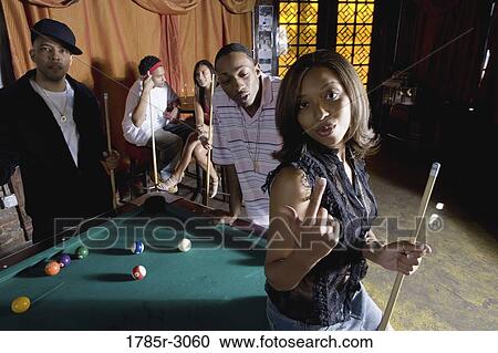 Young woman with pool stick next to pool table with friends watching in background View Large Photo Image Stock Image - Young woman with pool stick next to pool table with friends watching in background. Fotosearch