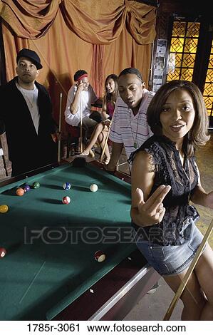 Young woman with pool stick next to pool table with friends watching in background View Large Photo Image Stock Image - Young woman with pool stick next to pool table with friends watching in background. Fotosearch
