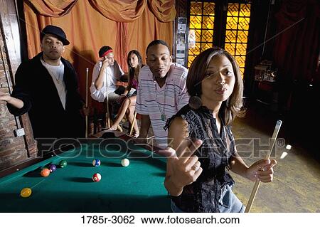 Young woman with pool stick next to pool table with friends watching in background View Large Photo Image Stock Image - Young woman with pool stick next to pool table with friends watching in background. Fotosearch