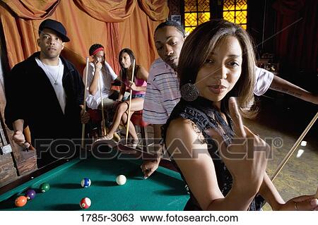 Young woman with pool stick next to pool table with friends watching in background View Large Photo Image Stock Image - Young woman with pool stick next to pool table with friends watching in background. Fotosearch