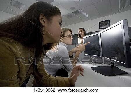 Stock Image - Young women looking at computer screen. Fotosearch