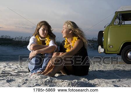 Young women sitting on sand at beach next to van View Large Photo Image Stock Photo - Young women sitting on sand at beach next to van. Fotosearch