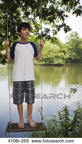 Stock Photography - Boy standing on swing by lake. Fotosearch