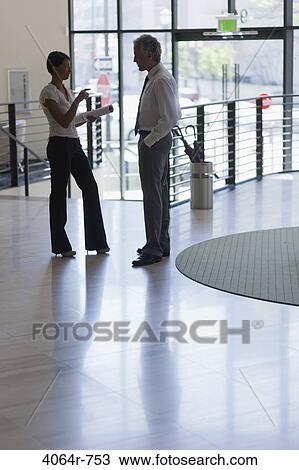 Businessman and businesswoman discussing in lobby of office View Large Photo Image Stock Image - Businessman and businesswoman discussing in lobby of office. Fotosearch