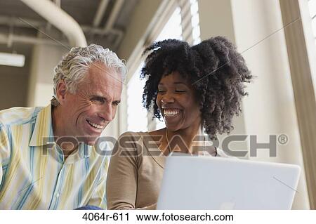 Stock Image - Businessman and woman using laptop in office. Fotosearch