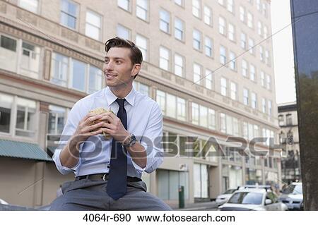 Stock Image - Businessman eating sandwich outside office building. Fotosearch