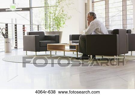 Businessman waiting in office lobby, using mobile phone View Large Photo Image Stock Photo - Businessman waiting in office lobby, using mobile phone. Fotosearch