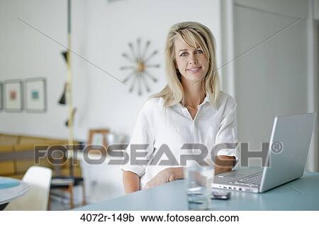 Businesswoman smiling while using a laptop at home View Large Photo Image Stock Image - Businesswoman smiling while using a laptop at home. Fotosearch
