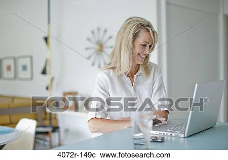 Stock Image - Businesswoman smiling while using a laptop at home. Fotosearch