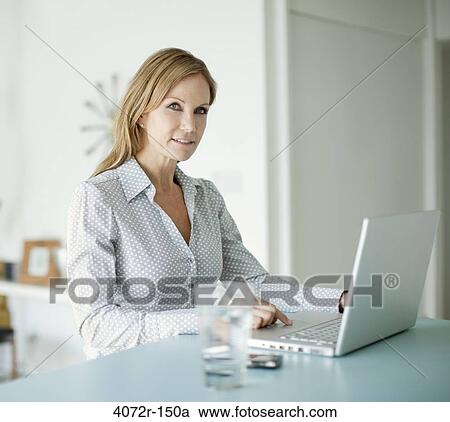 Businesswoman smiling while using a laptop at home View Large Photo Image Stock Image - Businesswoman smiling while using a laptop at home. Fotosearch