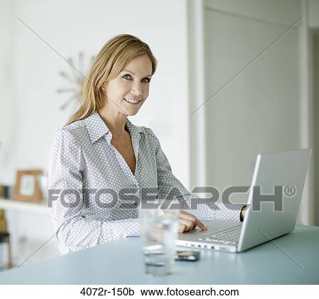 Businesswoman smiling while using a laptop at home View Large Photo Image Stock Image - Businesswoman smiling while using a laptop at home. Fotosearch