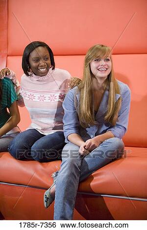 Cheerful teenage girlfriends sitting together on a couch View Large Photo Image Stock Photograph - Cheerful teenage girlfriends sitting together on a couch. Fotosearch