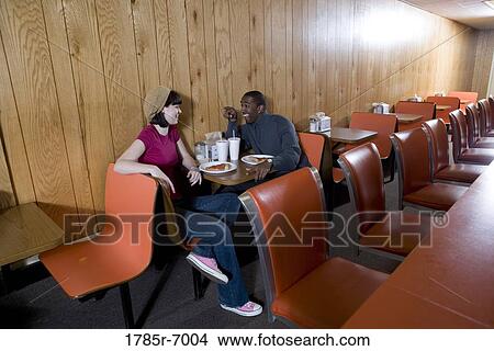 Picture - Cheerful young inter-racial couple sitting in a pizza parlor. Fotosearch