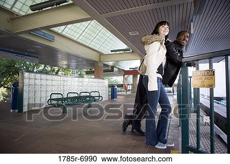 Cheerful young inter-racial couple waiting at the platform of a public train station View Large Photo Image Stock Image - Cheerful young inter-racial couple waiting at the platform of a public train station. Fotosearch