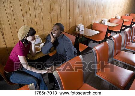 Stock Image - Cheerful young inter-racial couple sitting in a cafe. Fotosearch