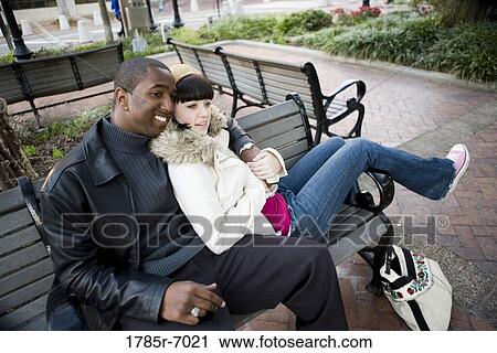 Cheerful young inter-racial couple sitting on a park bench View Large Photo Image Stock Image - Cheerful young inter-racial couple sitting on a park bench. Fotosearch