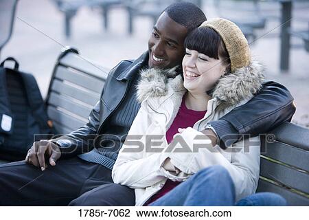 Cheerful young inter-racial couple embracing on a park bench View Large Photo Image Stock Image - Cheerful young inter-racial couple embracing on a park bench. Fotosearch