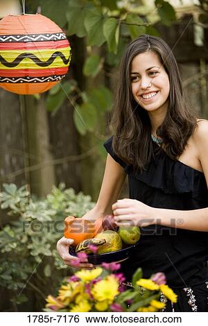 Cheerful young woman holding a bowl of fruit View Large Photo Image Stock Photograph - Cheerful young woman holding a bowl of fruit. Fotosearch