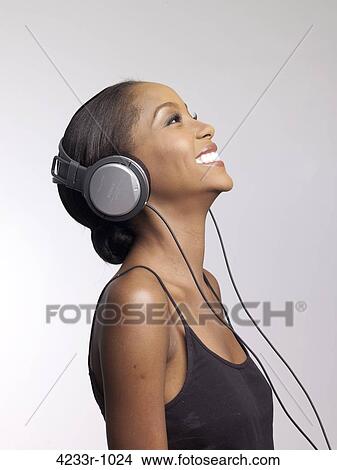 Cheerful young woman listening to headphones over colored background View Large Photo Image Picture - Cheerful young woman listening to headphones over colored background. Fotosearch