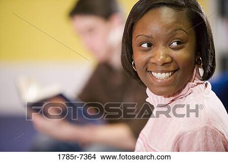 Close-up of a cheerful teenage girl with teenage boy reading in background View Large Photo Image Picture - Close-up of a cheerful teenage girl with teenage boy reading in background. Fotosearch