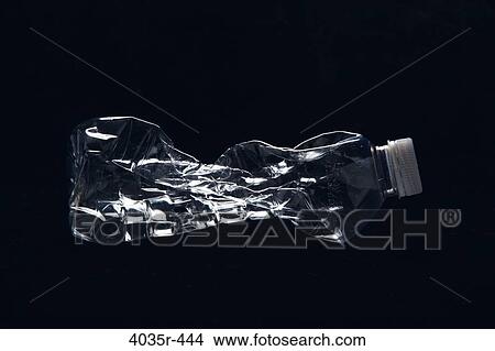 Picture - Close-up of a crushed plastic water bottle against black background. Fotosearch