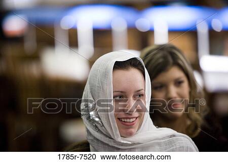 Stock Image - Close-up of a smiling young woman wearing a head scarf, another woman in the background. Fotosearch