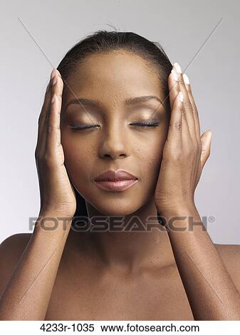 Stock Photography - Close-up of a woman holding head with eyes closed over colored background. Fotosearch