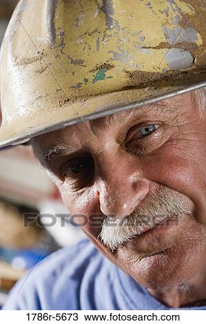 Stock Image - Close-up of senior man wearing hard hat. Fotosearch