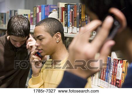 Stock Photo - Close-up view of three teenage boys talking on cell phones in a library. Fotosearch