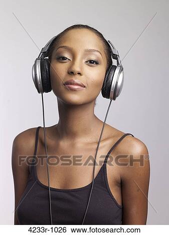 Stock Photograph - Confident young woman listening to headphones over colored background. Fotosearch