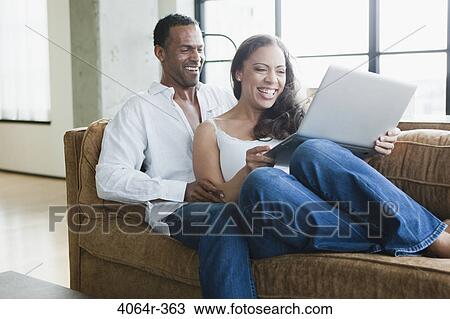Couple sitting on couch and using laptop View Large Photo Image Stock Image - Couple sitting on couch and using laptop. Fotosearch