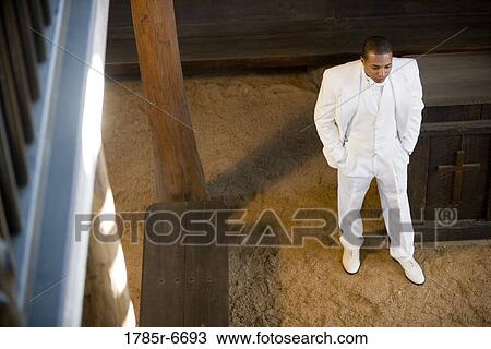 Stock Image - Elevated view of a groom in a white tuxedo pacing with hands in pockets. Fotosearch