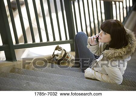 Elevated view of a young woman holding cellphone sitting on concrete steps View Large Photo Image Stock Image - Elevated view of a young woman holding cellphone sitting on concrete steps. Fotosearch
