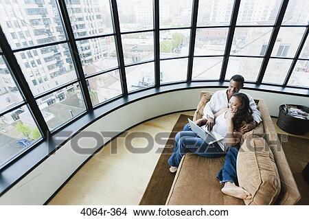 Picture - Elevated view of couple sitting on couch in loft apartment and using laptop. Fotosearch