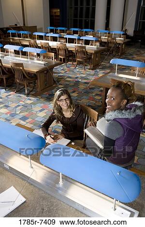 Elevated view of two women students sitting in the reading room of a library View Large Photo Image Stock Photo - Elevated view of two women students sitting in the reading room of a library. Fotosearch