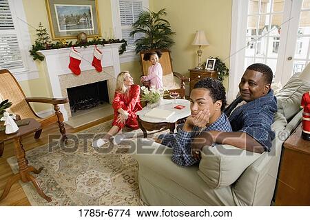 Family in pajamas sitting in living room decorated for Christmas View Large Photo Image Picture - Family in pajamas sitting in living room decorated for Christmas. Fotosearch