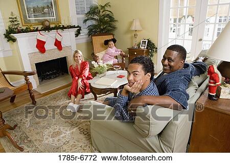 Stock Image - Family in pajamas sitting in living room decorated for Christmas. Fotosearch