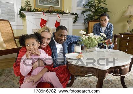 Stock Image - Family in pajamas sitting in living room decorated for Christmas. Fotosearch