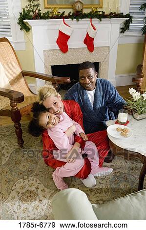 Stock Photo - Family in pajamas sitting in living room decorated for Christmas. Fotosearch