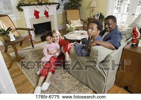 Stock Photography - Family in pajamas sitting in living room decorated for Christmas. Fotosearch