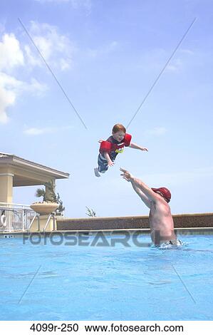Stock Image - Father throwing son swimming in outdoor pool. Fotosearch