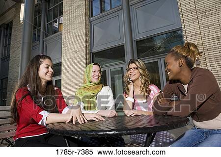 Four young women sitting at a table outside a building, socializing and conversing View Large Photo Image Stock Photography - Four young women sitting at a table outside a building, socializing and conversing. Fotosearch