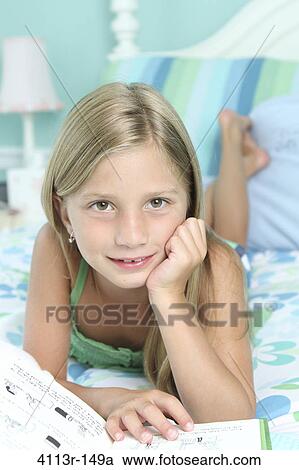 Stock Image - Girl lying on the bed and reading a book. Fotosearch