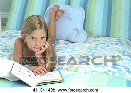 Stock Image - Girl lying on the bed and reading a book. Fotosearch