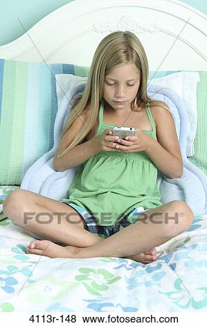 Girl sitting on the bed and text messaging on a mobile phone View Large Photo Image Stock Photo - Girl sitting on the bed and text messaging on a mobile phone. Fotosearch