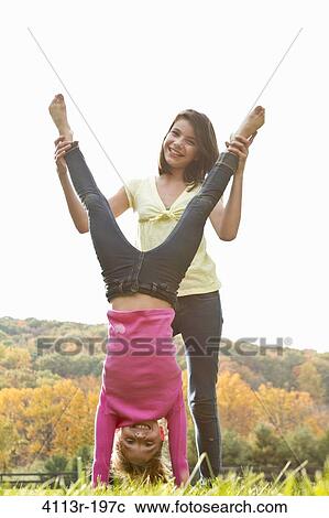 Stock Image - Girls helping friend doing handstand in field. Fotosearch