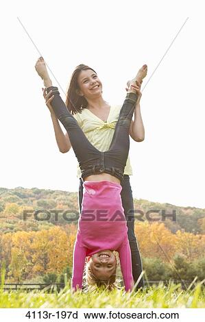 Stock Image - Girls helping friend doing handstand in field. Fotosearch